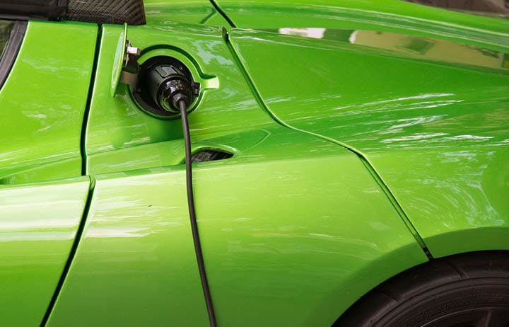 Green electric car charging: Close-up of indistinguishable electric car 'fueling', i.e. plugged to the electricity hose, charging battery.